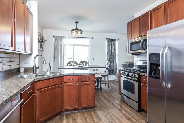 kitchen with a sink, a peninsula, stainless steel appliances, dark wood-type flooring, and backsplash