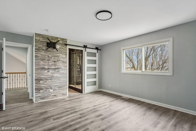 unfurnished bedroom featuring wood finished floors, baseboards, and a barn door