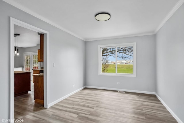 empty room with crown molding, light wood-style flooring, and baseboards