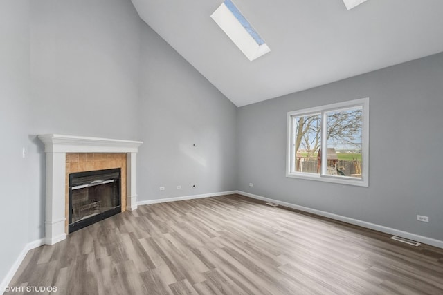 unfurnished living room with wood finished floors, a tile fireplace, visible vents, and lofted ceiling with skylight