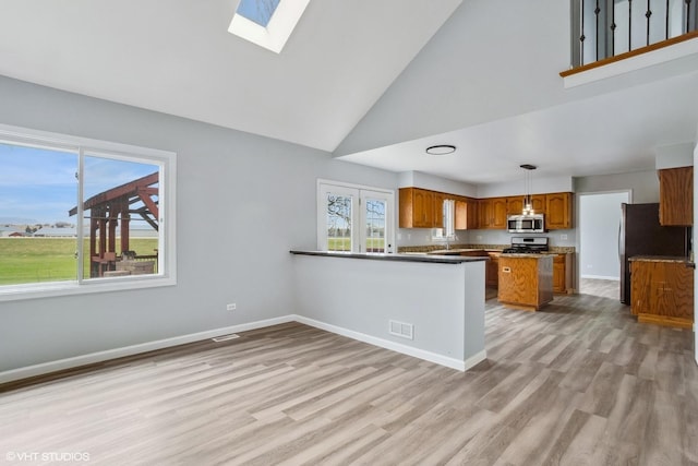 kitchen featuring high vaulted ceiling, visible vents, a skylight, appliances with stainless steel finishes, and brown cabinets