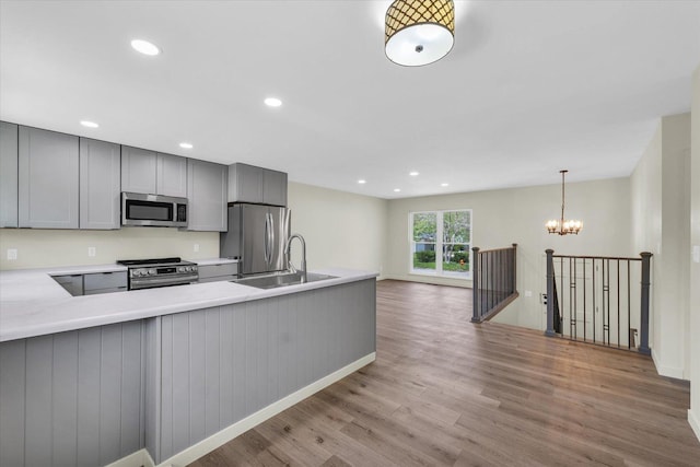 kitchen featuring stainless steel appliances, a sink, light wood-type flooring, gray cabinetry, and light countertops
