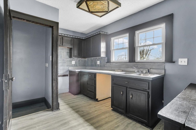 kitchen with backsplash, light countertops, light wood-type flooring, and a sink