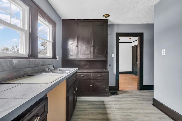 kitchen with a textured ceiling, a sink, dark brown cabinets, baseboards, and light wood-style floors