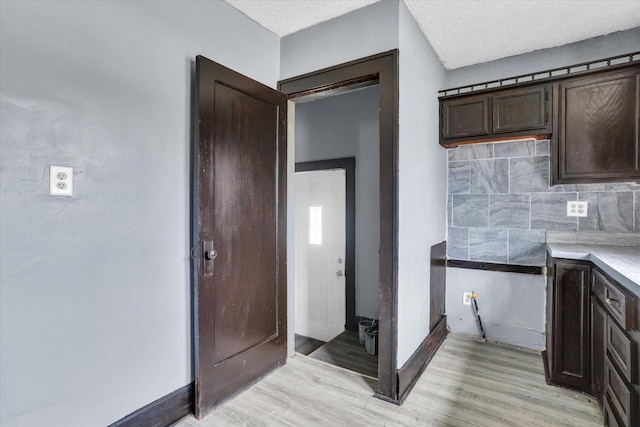 kitchen with decorative backsplash, light wood-type flooring, dark brown cabinetry, light countertops, and baseboards