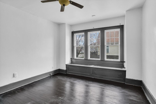 spare room with baseboards, ceiling fan, and dark wood-style flooring