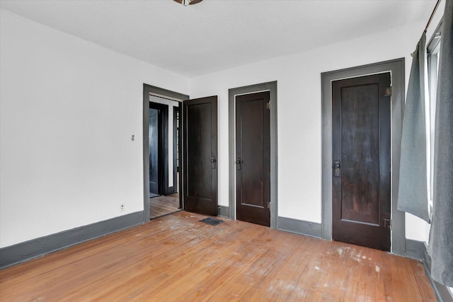 unfurnished bedroom featuring visible vents, hardwood / wood-style flooring, and baseboards