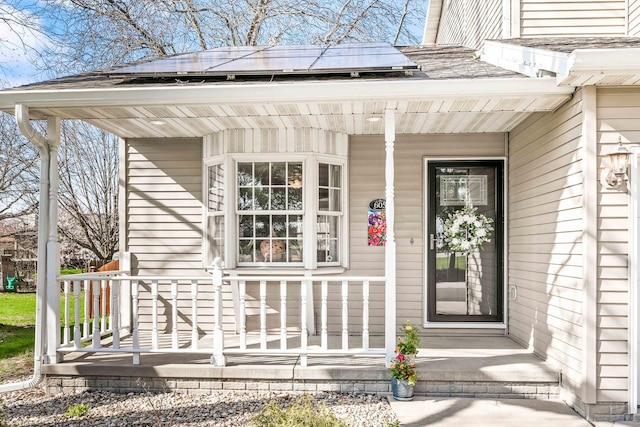 view of exterior entry with solar panels, a porch, and a shingled roof