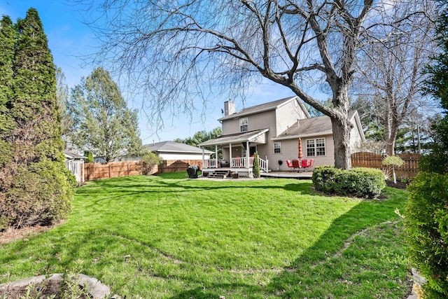 back of property with a chimney, a wooden deck, a yard, and a fenced backyard