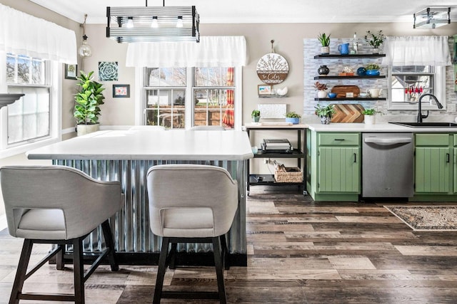 kitchen featuring stainless steel dishwasher, a sink, green cabinetry, dark wood finished floors, and ornamental molding