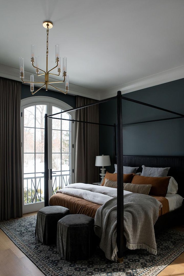 bedroom featuring access to exterior, an inviting chandelier, crown molding, and wood finished floors