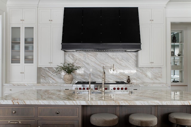 kitchen featuring tasteful backsplash, white cabinets, light stone counters, and a breakfast bar area