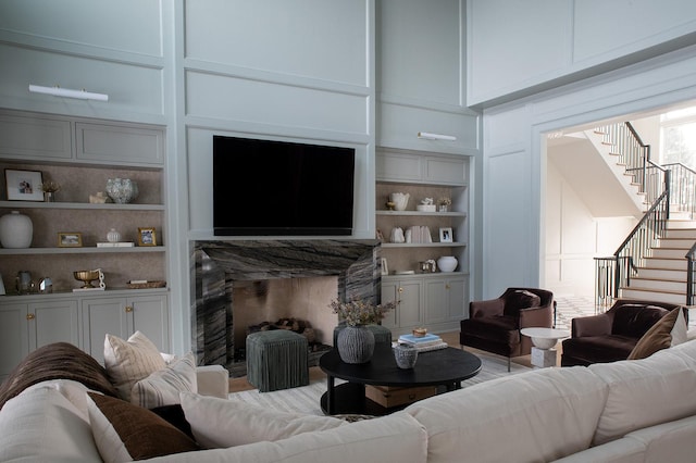 living room featuring a premium fireplace, built in features, a decorative wall, and stairway