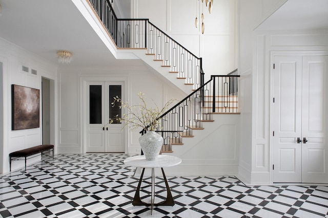 foyer entrance featuring a decorative wall, stairway, visible vents, and a towering ceiling