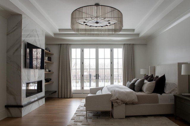 bedroom featuring a raised ceiling, wood finished floors, a tiled fireplace, and multiple windows