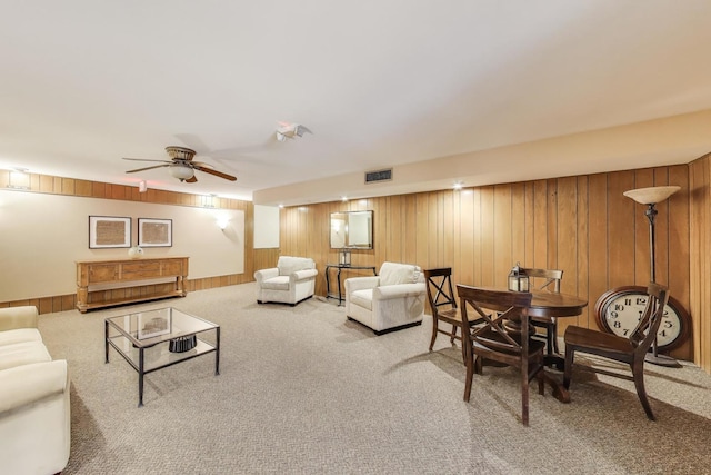 living area featuring carpet, visible vents, a ceiling fan, and wooden walls