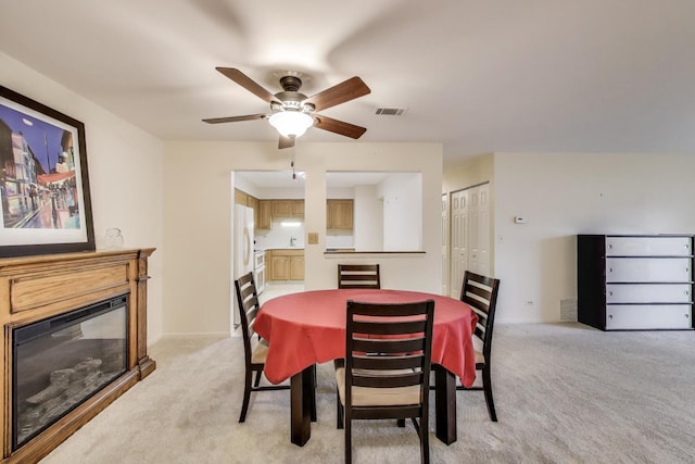 dining area featuring light carpet, ceiling fan, a glass covered fireplace, and visible vents