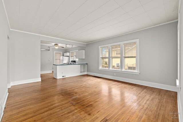 unfurnished living room with baseboards, ornamental molding, and hardwood / wood-style flooring