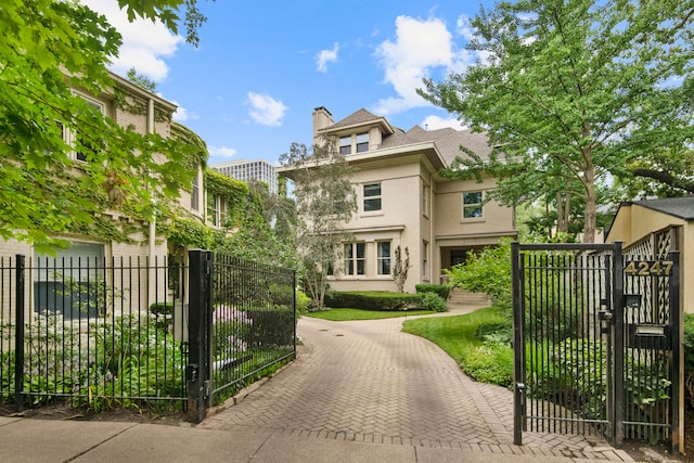 view of front of property with a chimney, stucco siding, fence, and a gate