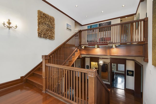 stairs featuring wood finished floors, baseboards, ornamental molding, and a towering ceiling