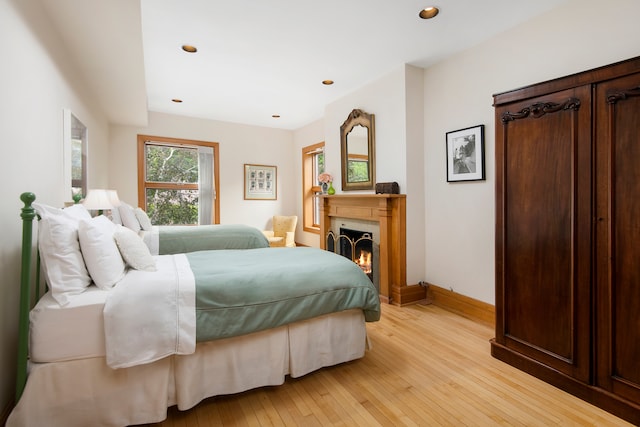 bedroom with a warm lit fireplace, baseboards, recessed lighting, and light wood-style floors