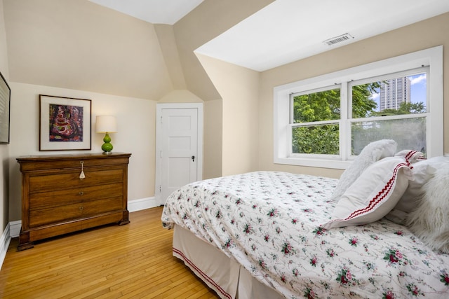 bedroom with light wood finished floors, visible vents, baseboards, and lofted ceiling