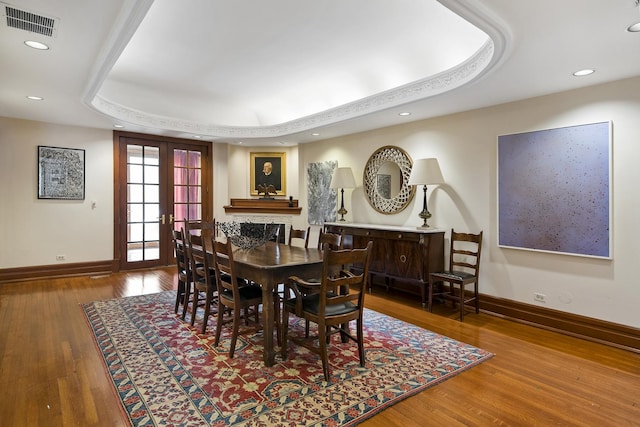 dining area featuring hardwood / wood-style flooring, baseboards, and a raised ceiling