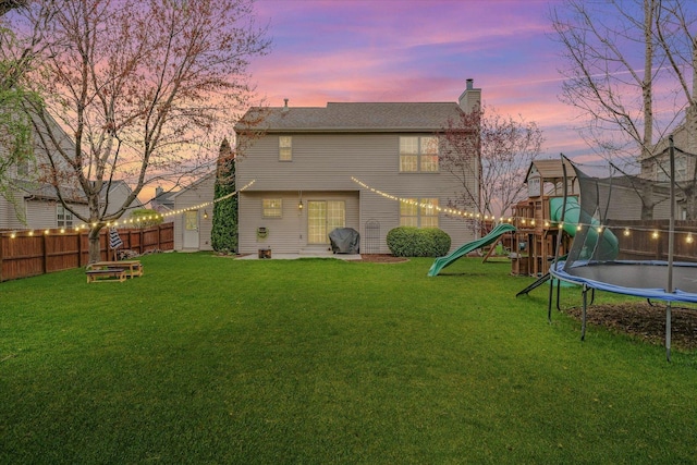 3410 Waterville Ct, Champaign, IL 61822 - back of house at dusk featuring a fenced backyard, a playground, a chimney, a trampoline, and a yard
