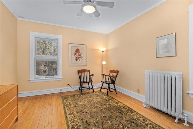 sitting room with radiator heating unit, hardwood / wood-style floors, ceiling fan, and crown molding
