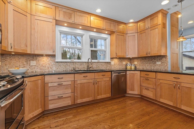kitchen featuring wood finished floors, a sink, dark stone counters, decorative backsplash, and appliances with stainless steel finishes