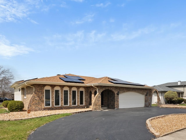 view of front facade with brick siding, solar panels, a garage, and driveway