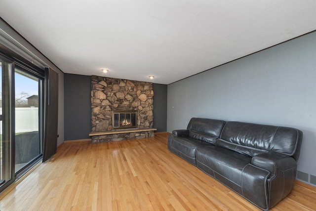living room featuring light wood-style flooring, a stone fireplace, and visible vents