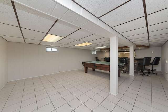below grade area with baseboards, billiards, light tile patterned flooring, wood walls, and a drop ceiling