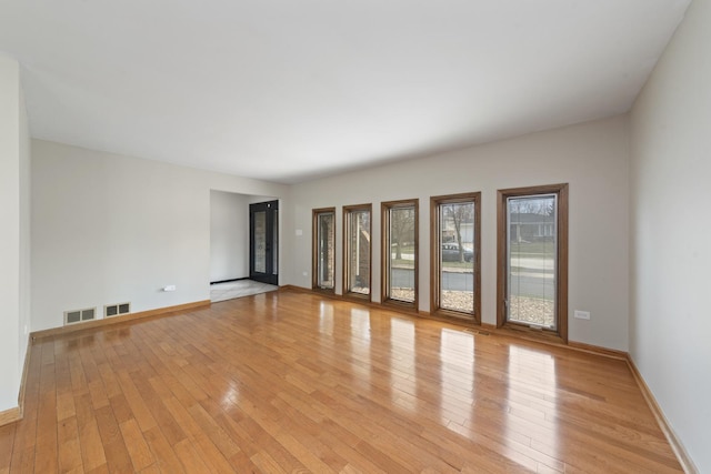 spare room with light wood finished floors, visible vents, and baseboards