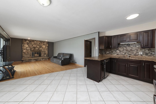 kitchen with tasteful backsplash, open floor plan, dark brown cabinets, dark stone counters, and a sink