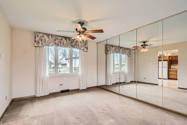 unfurnished bedroom with freestanding refrigerator, carpet, a ceiling fan, visible vents, and baseboards