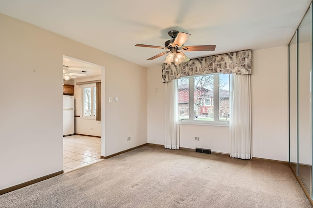 empty room featuring light carpet, plenty of natural light, visible vents, and a ceiling fan