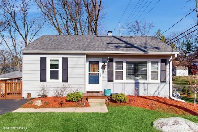 bungalow featuring a front lawn, a shingled roof, and a chimney