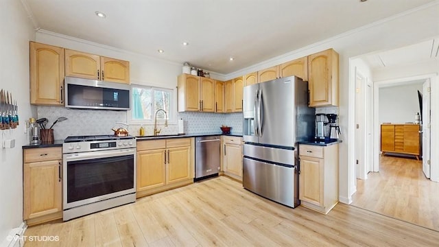 kitchen with dark countertops, stainless steel appliances, light wood finished floors, a sink, and light brown cabinetry