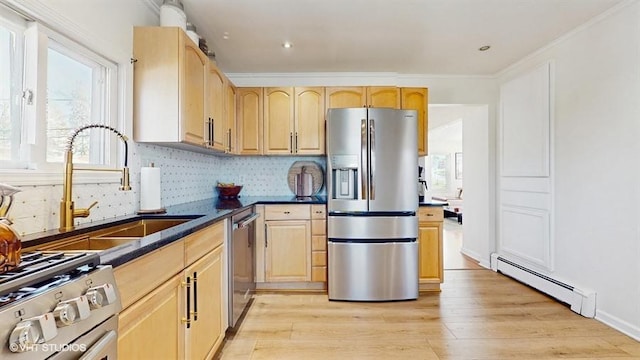 kitchen with a sink, appliances with stainless steel finishes, light brown cabinets, and baseboard heating