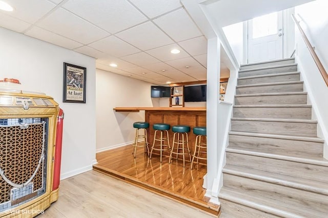 bar featuring recessed lighting, a bar, stairway, wood finished floors, and baseboards