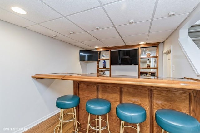 bar with a bar, baseboards, a drop ceiling, and wood finished floors