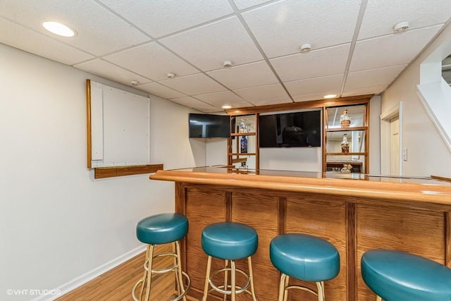 bar featuring a paneled ceiling, recessed lighting, a bar, wood finished floors, and baseboards