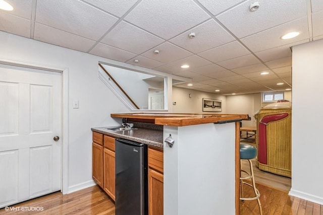 kitchen featuring a sink, light wood-type flooring, a peninsula, refrigerator, and a breakfast bar area