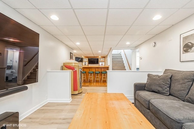 living area featuring a dry bar, a drop ceiling, wood finished floors, and stairs
