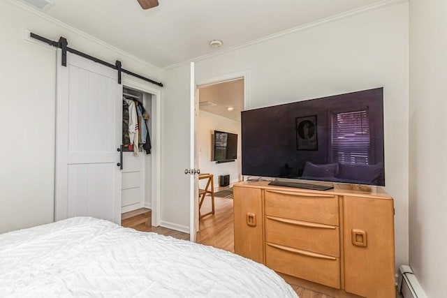 bedroom with baseboards, a barn door, ornamental molding, light wood-style floors, and a baseboard heating unit