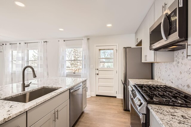 kitchen featuring tasteful backsplash, a sink, appliances with stainless steel finishes, light wood-style floors, and recessed lighting