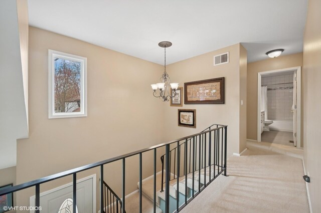 stairs with an inviting chandelier, carpet floors, visible vents, and baseboards