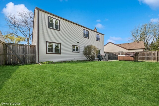 back of house with a hot tub, a lawn, a chimney, and a fenced backyard