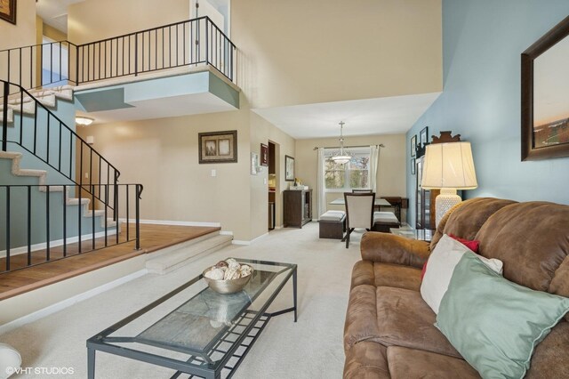 carpeted living room featuring stairway, baseboards, a notable chandelier, and a towering ceiling
